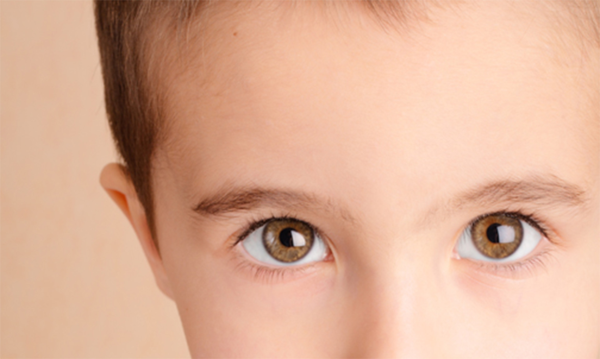 A close-up image of a child with brown eyes, looking directly at the camera.