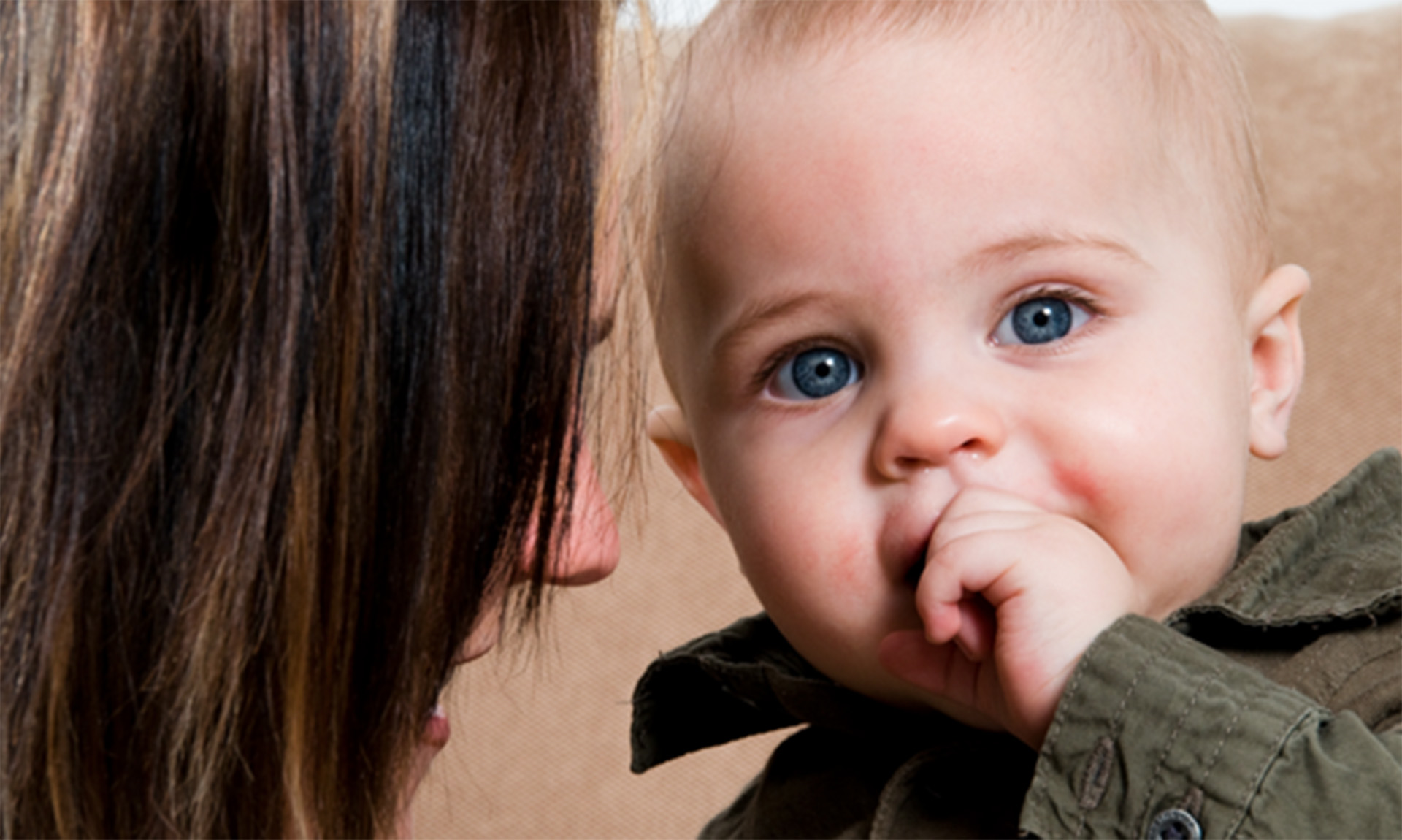 A close-up headshot of an adult and a child. The adult is on the left, and is visible in profile, while the child is on the right, and is looking toward the camera.