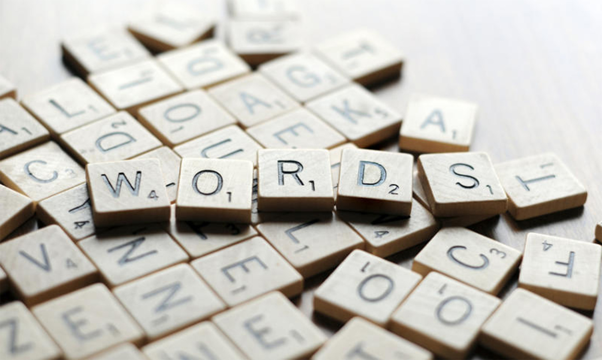 An image of small wooden tiles with letters on each tile, similar to the tiles from the board game Scrabble. There are two layers of tiles. The top layer spells out "WORDS".