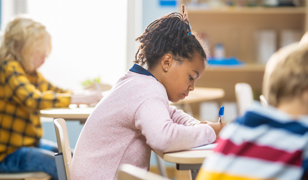 Young girl writes in notebook in elementary school classroom