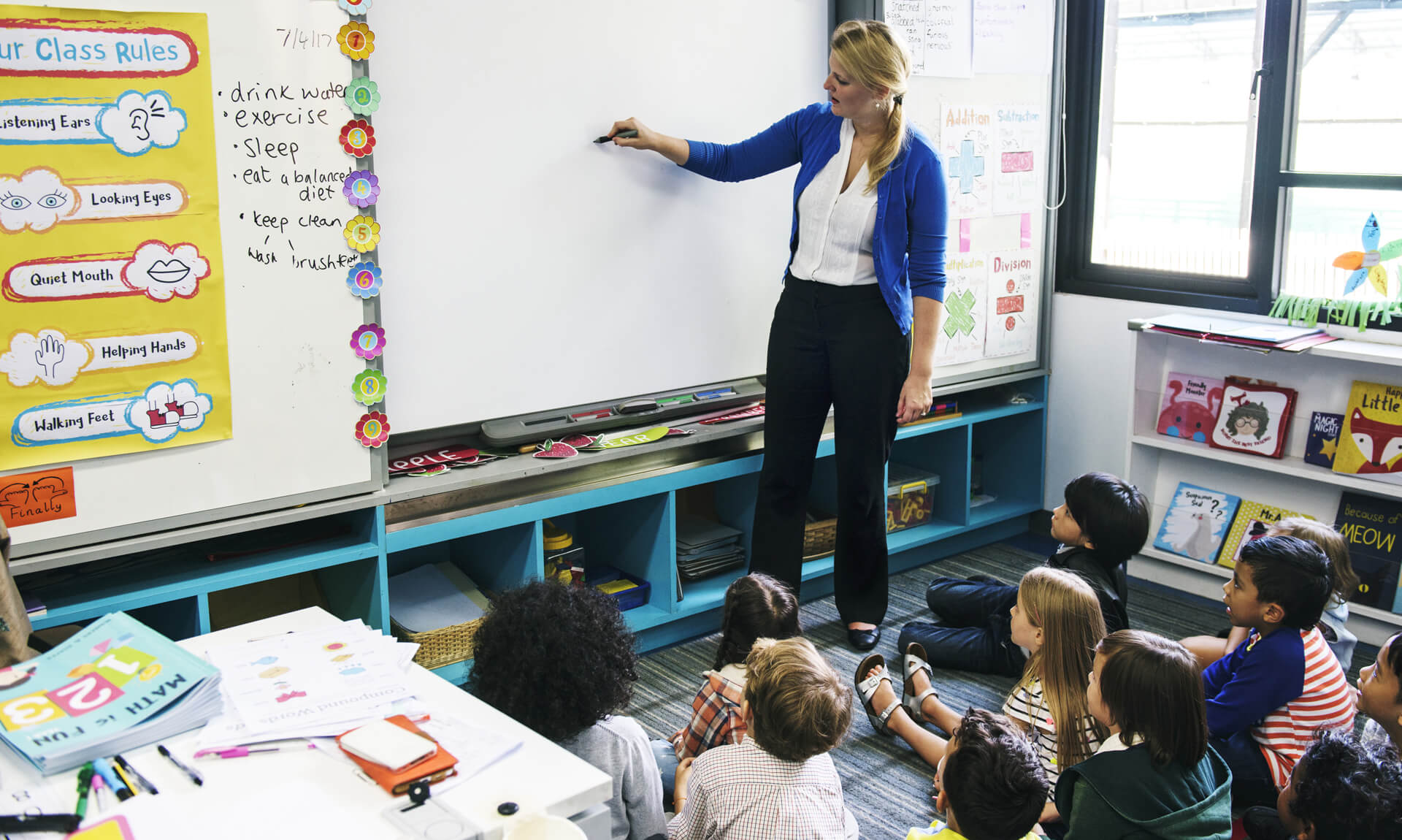 Teacher writes on white board in front of a class of elementary school children.
