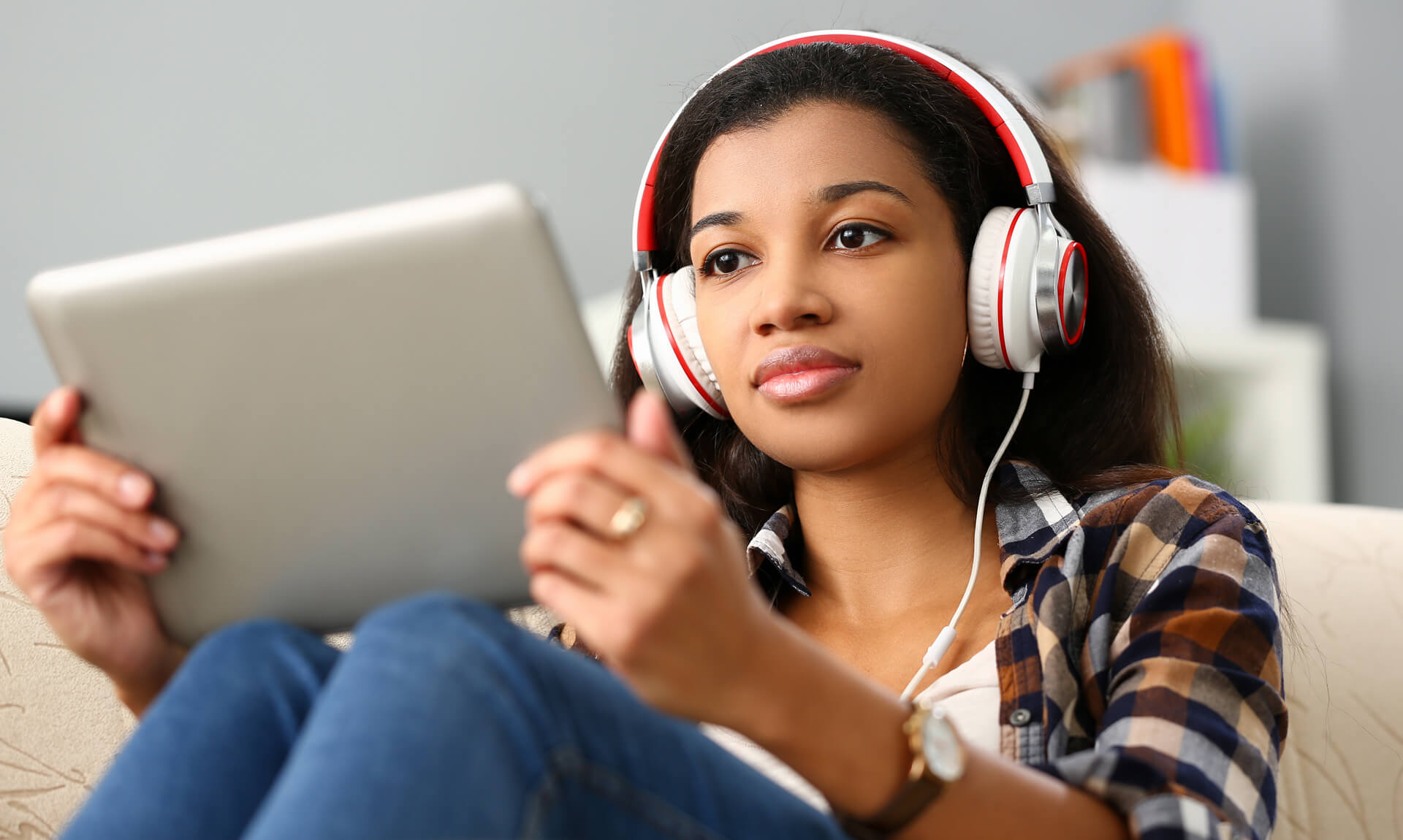 Teen age woman wearing red and white headphones looks at a table screen.