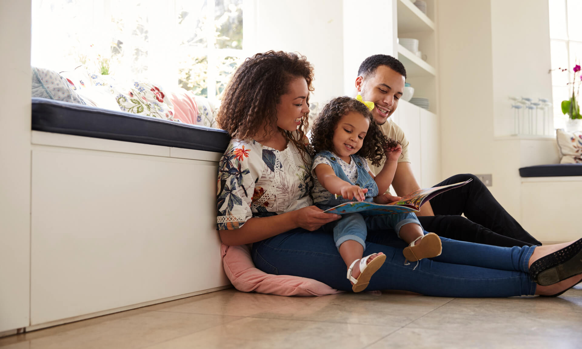 Parents and their daughter sitting on the floor reading a book