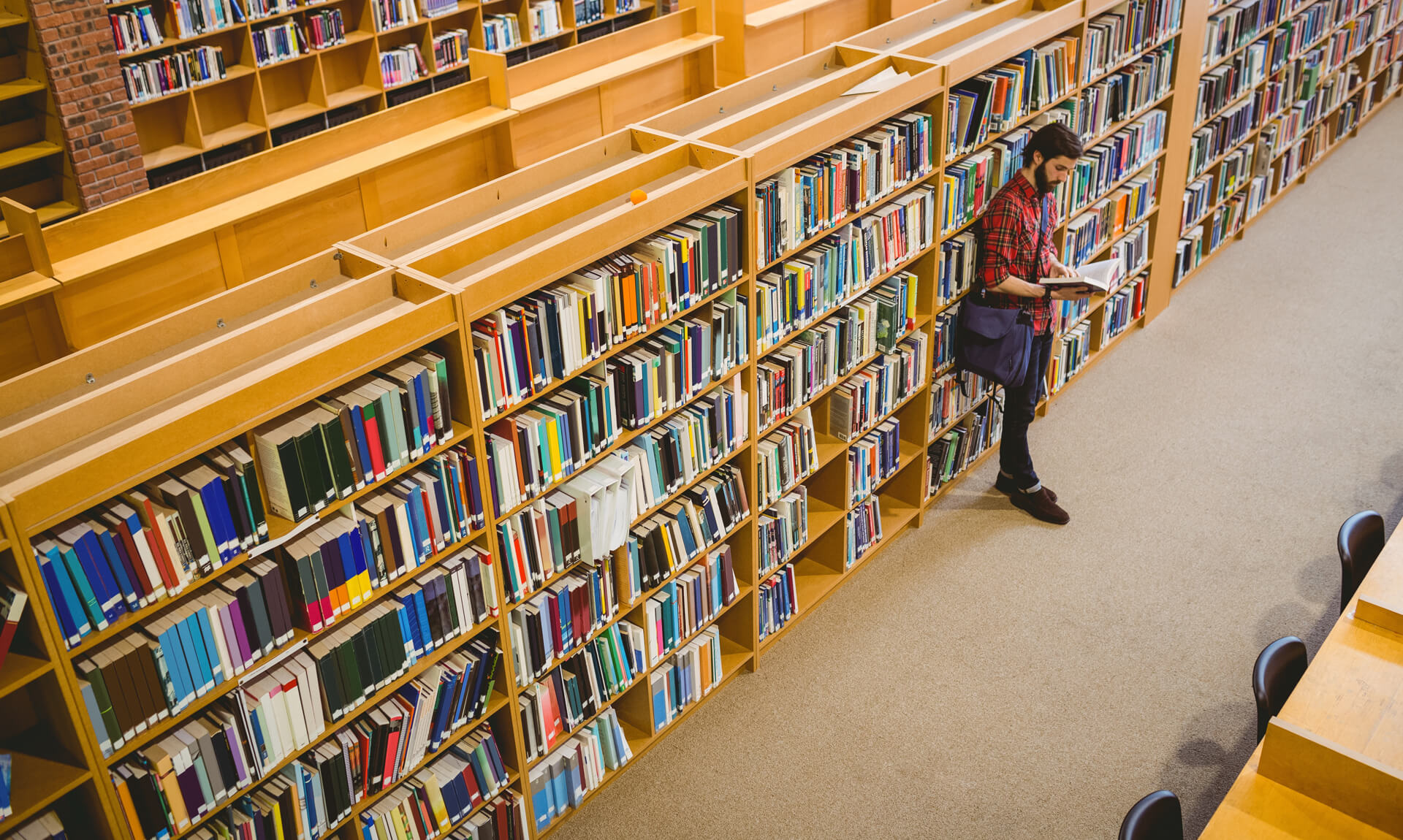 Student reading a book from shelf in library.