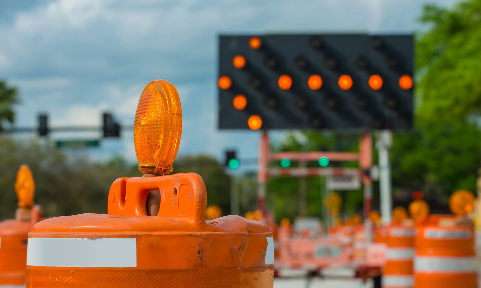 Close-up of traffic barrel with a roadwork scene and detour arrow in background