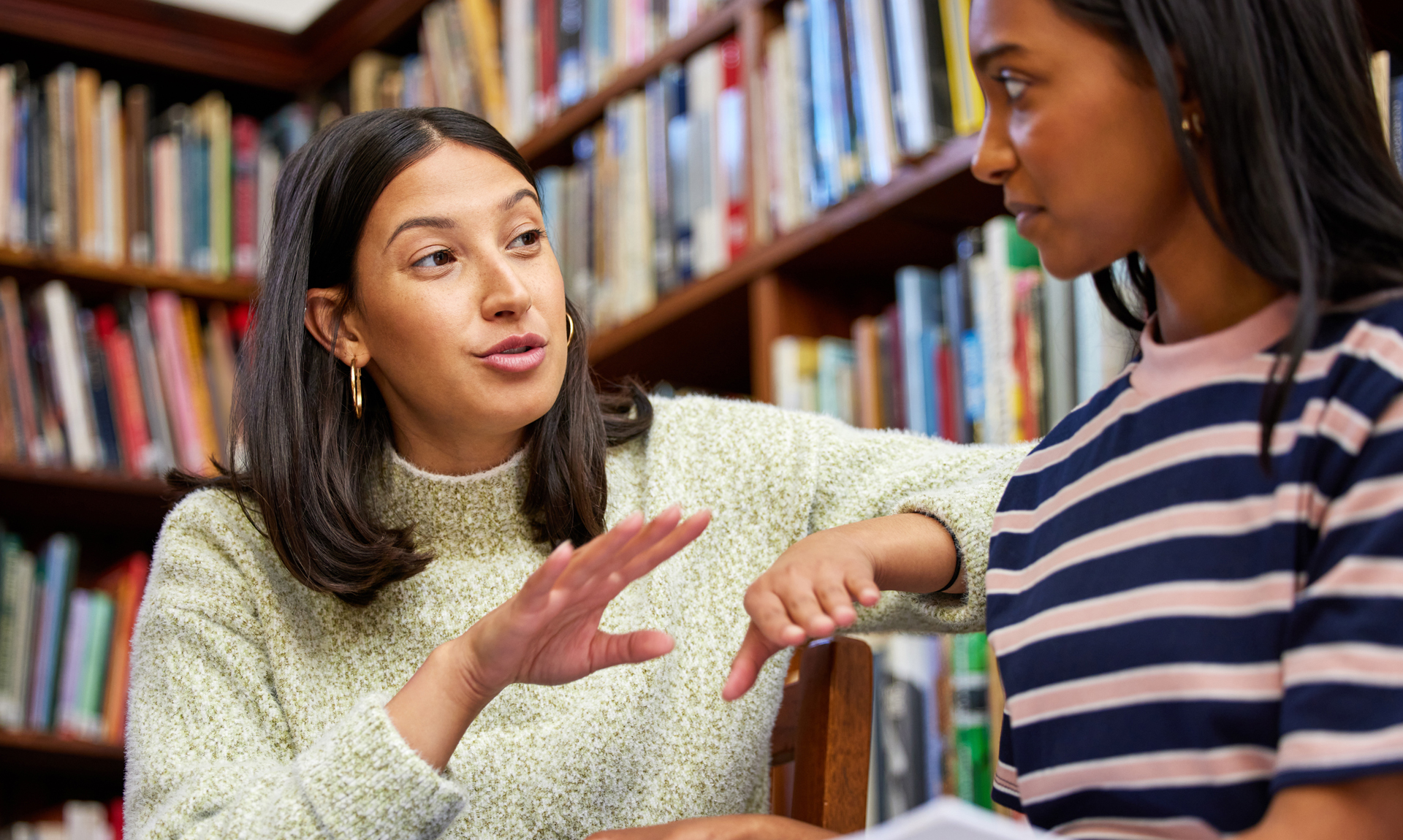 student and teacher sitting in a library discussing an assignment