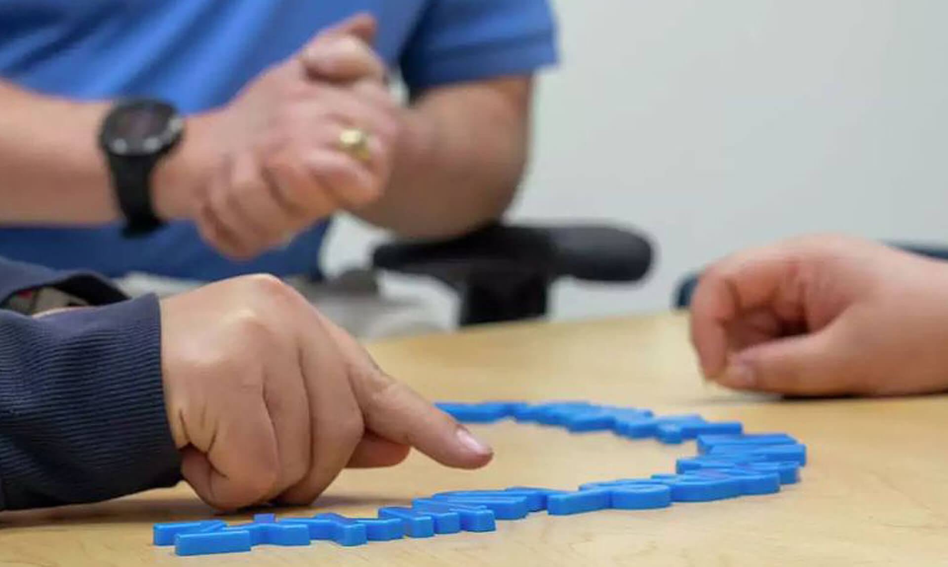 Hand pointing at plastic letters lined up on a tabletop.